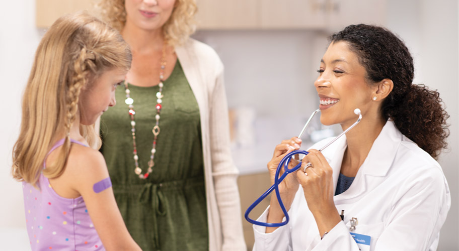 Image of a doctor putting on her stethoscope to check on a young girl.
