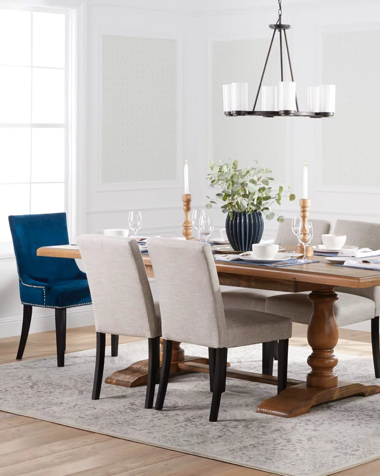 A transitional dining room with a beautiful wooden trestle table, upholstered seating, blue velvet end chairs, an industrial chandelier and a dining table area rug. Links to Daily Saves's dining room furniture and decor